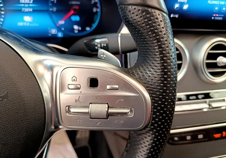 Gros plan sur le volant cuir perforé côté gauche du Mercedes GLC 300 e AMG Line, avec commandes intégrées et tableau de bord digital.