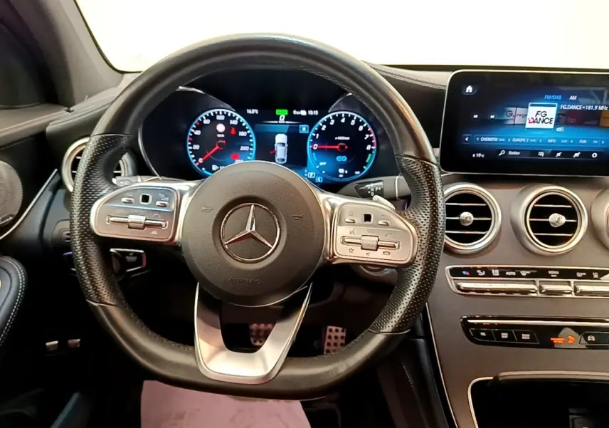 Vue intérieure centrée sur le volant cuir AMG et le tableau de bord numérique du Mercedes GLC 300 e blanc de 2020.
