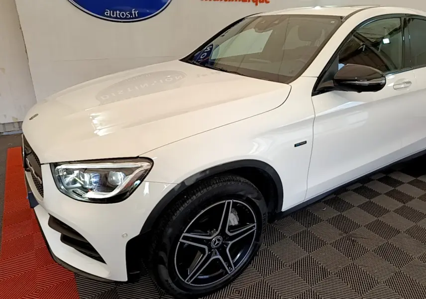 Mercedes GLC 300 e AMG Line blanc vu de 3/4 avant droit, avec jantes noires et phares LED allumés.