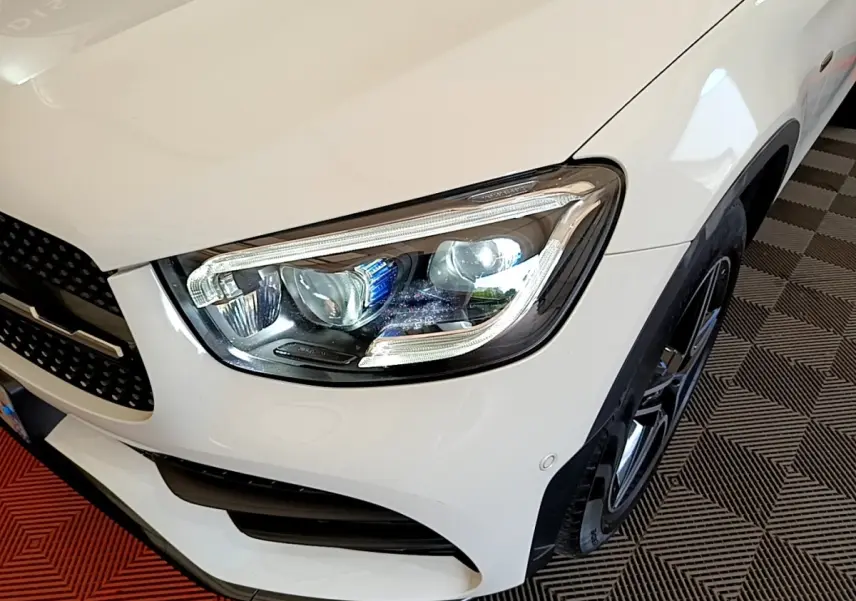 Gros plan sur l'avant droit blanc du Mercedes GLC Coupé 300 e AMG Line, mettant en valeur le phare LED et la jante noire.