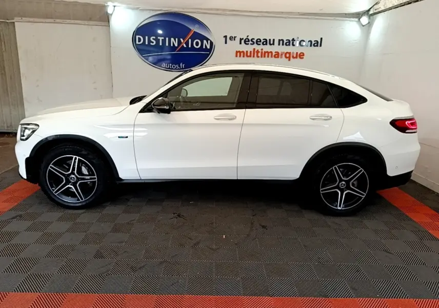 Profil droit d’un Mercedes GLC Coupé blanc hybride rechargeable avec jantes AMG et feux arrière LED allumés.