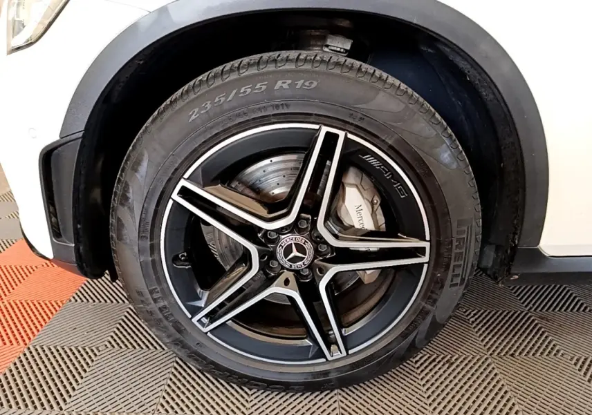 Gros plan sur la roue avant gauche noire et argentée d’un Mercedes GLC 300 e AMG Line blanc, avec logo AMG visible.
