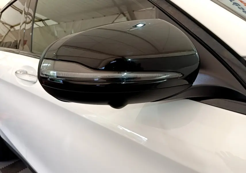 Gros plan sur le rétroviseur noir côté gauche d’un Mercedes GLC Coupé blanc, avec clignotant intégré.