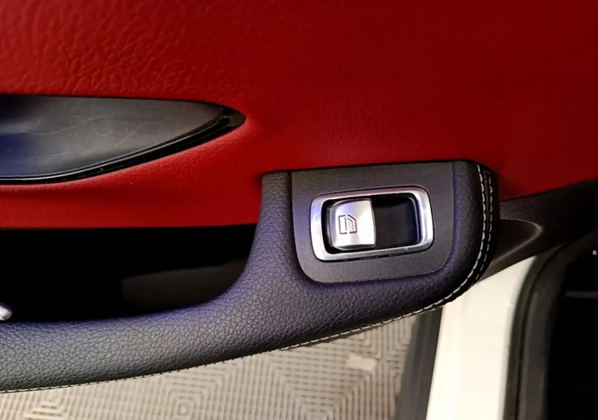 Gros plan sur la poignée intérieure noire avec bouton de vitre, contreporte rouge du Mercedes GLC Coupé blanc 2020.