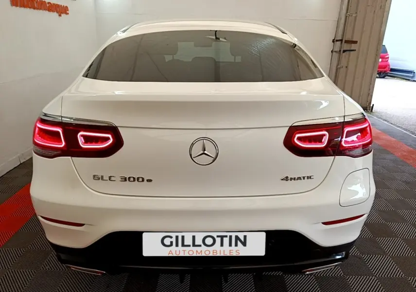Vue arrière d'un Mercedes GLC 300 e AMG Line 4Matic blanc avec feux LED allumés en intérieur showroom.