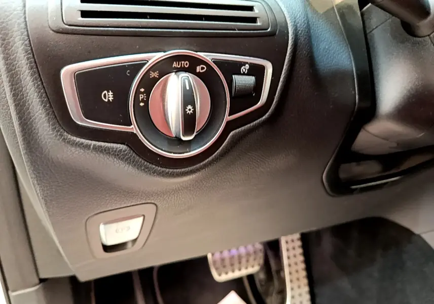 Gros plan sur la commande des phares et frein à main électrique côté gauche du tableau de bord du Mercedes GLC 300 e AMG Line blanc.