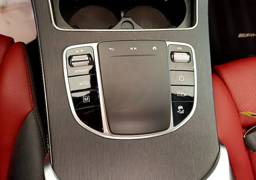 Gros plan sur la console centrale en bois avec commandes tactiles et sièges cuir rouge du Mercedes GLC 300 e AMG Line.