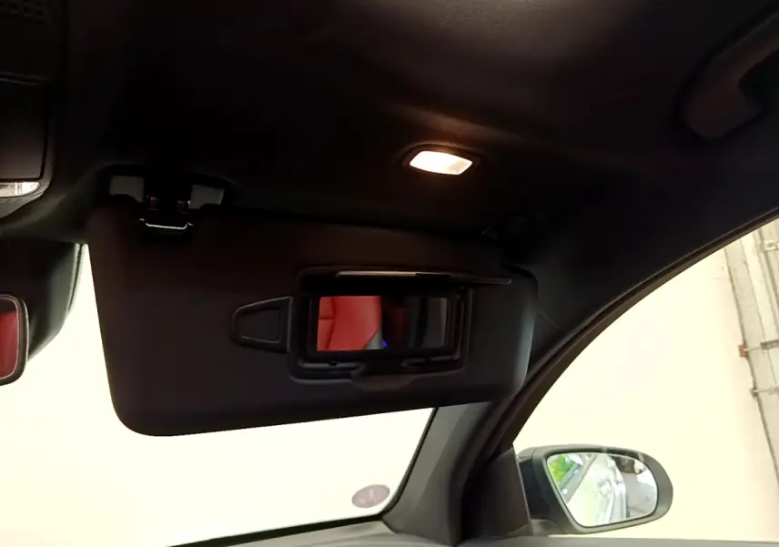 Intérieur du Mercedes GLC Coupé 300 e AMG Line 2020, vue du pare-soleil côté conducteur avec miroir éclairé et siège rouge en reflet.