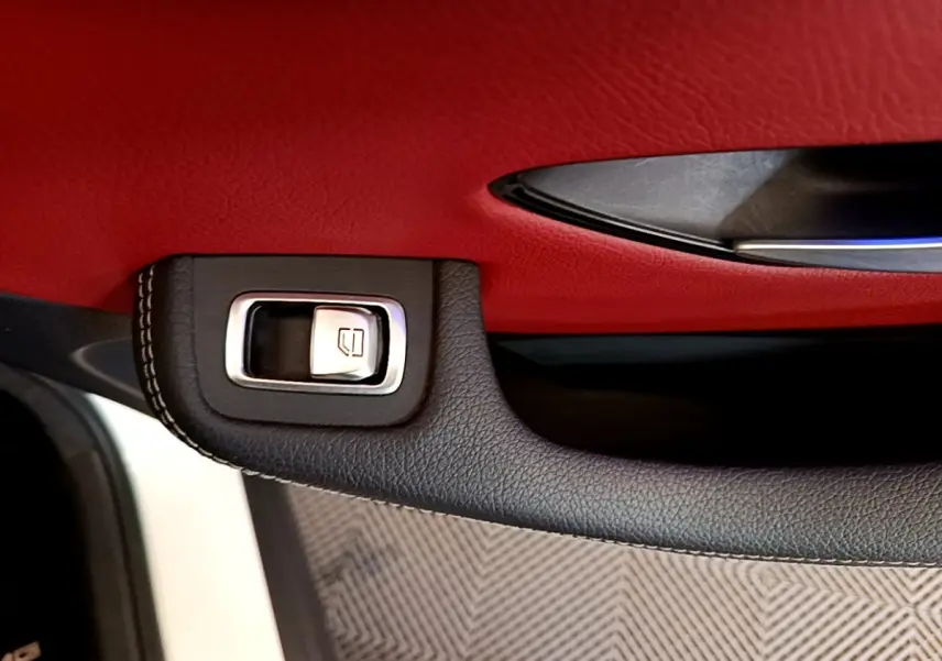 Gros plan sur la poignée intérieure noire et bouton de lève-vitre, avec garniture rouge du panneau de porte du Mercedes GLC Coupé blanc.