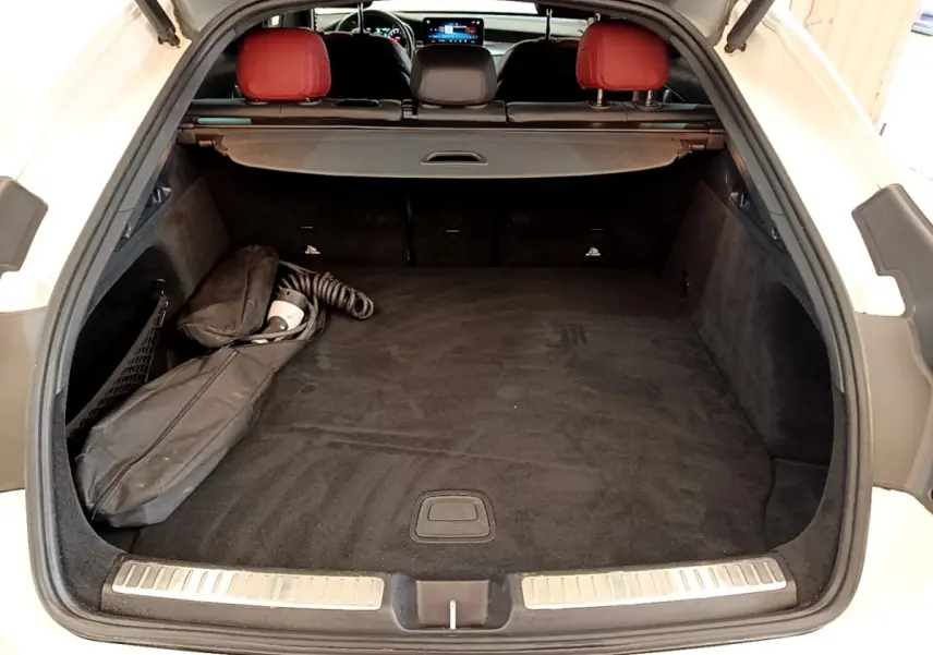 Vue arrière du coffre ouvert d'un Mercedes GLC Coupé blanc avec intérieur noir et appuis-tête rouges visibles.