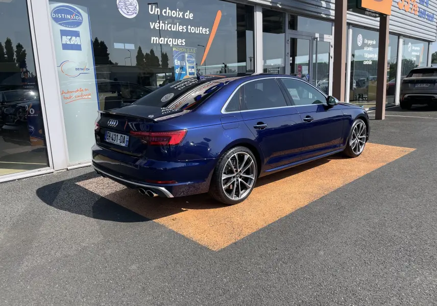 Audi S4 bleu Navarre vue 3/4 arrière droit, avec jantes alliage et double sortie d'échappement chromée, stationnée devant un showroom.