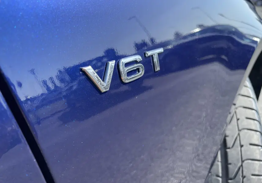 Gros plan sur l’inscription V6T en chrome sur la carrosserie bleu Navarre de l’Audi S4, avec une partie du pneu visible.