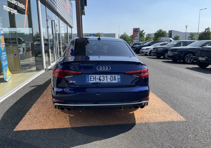 Vue arrière d'une Audi S4 bleu Navarre garée devant un showroom, avec ses quatre sorties d'échappement visibles.