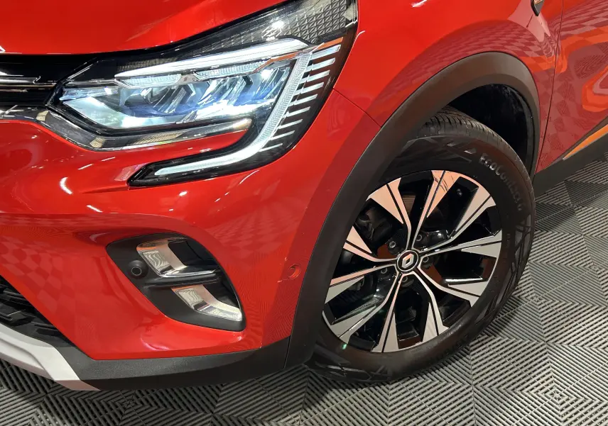Gros plan sur l'avant droit du Renault Captur rouge flamme, mettant en valeur le phare LED et la jante alliage bicolore.