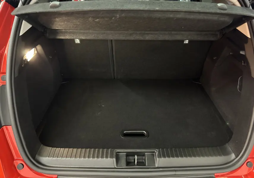 Coffre ouvert vu de l'arrière d'un Renault Captur rouge flamme métal, montrant un espace de chargement propre et éclairé.
