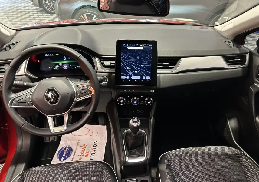 Vue intérieure avant du Renault Captur rouge flamme métal 2024, avec tableau de bord numérique et écran tactile vertical.