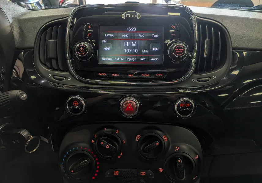 Tableau de bord noir brillant de la Fiat 500 1.2 69 CH Lounge avec écran radio et commandes climatiques visibles.