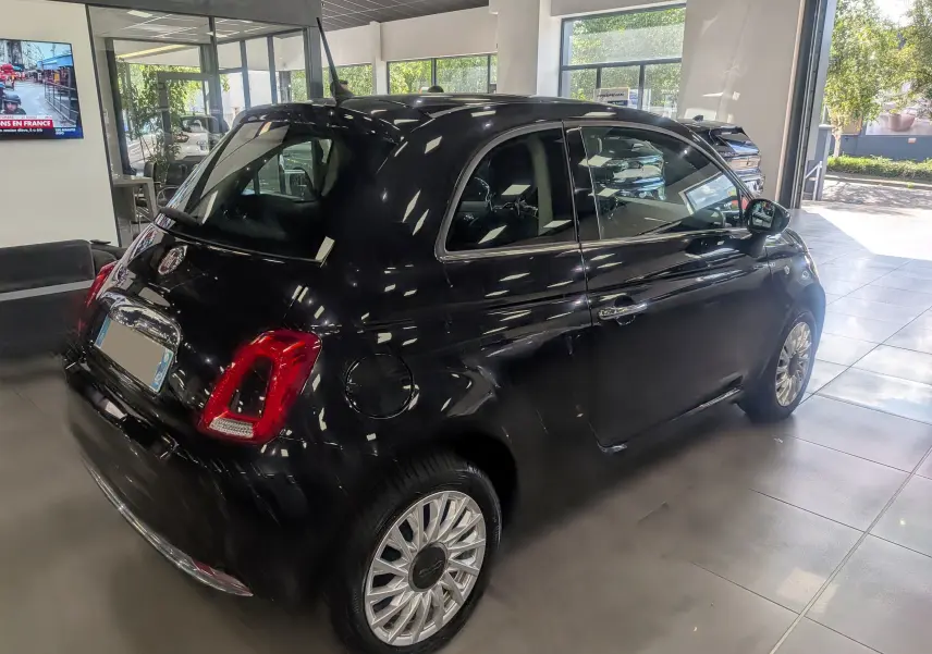 Fiat 500 1.2 69 CH Lounge noire vue 3/4 arrière droit en intérieur avec jantes alliage et feux arrière rouges.