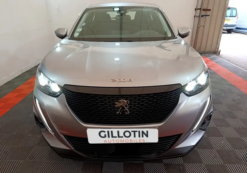 Vue de face d'une Peugeot 2008 gris clair avec phares LED allumés dans un garage fermé.