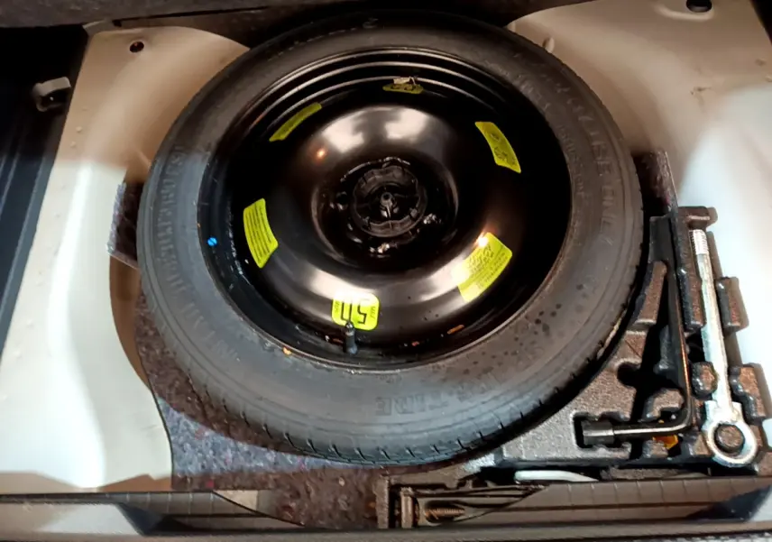 Vue rapprochée de la roue de secours noire avec outils de bord dans le coffre d'une Peugeot 2008 gris clair.