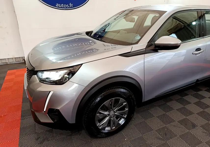 Vue 3/4 avant gauche d'un Peugeot 2008 gris clair avec phares LED et jantes alliage en intérieur showroom.