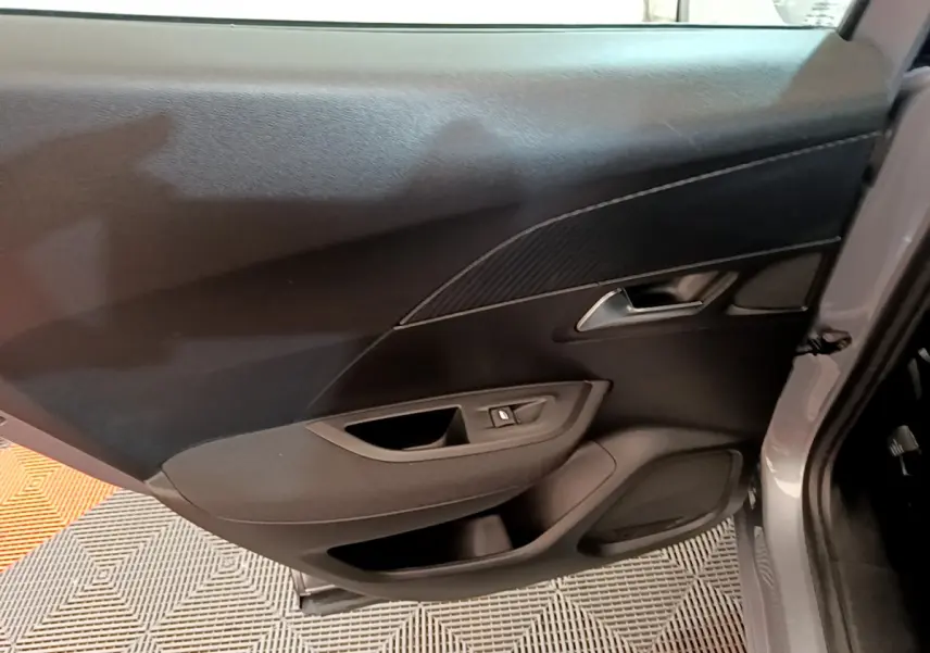 Intérieur de la porte arrière gauche d'une Peugeot 2008 gris clair, avec poignée et commande de vitre électrique.