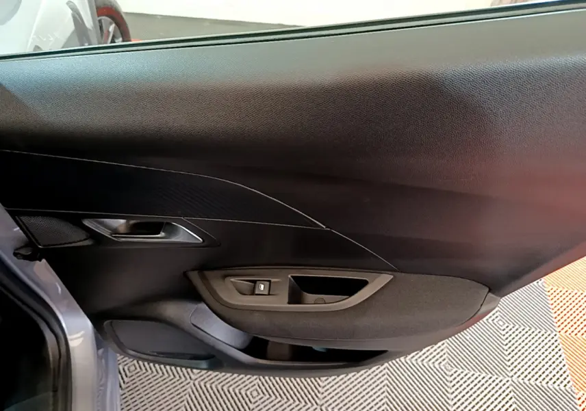 Intérieur de la porte côté gauche d'une Peugeot 2008 gris clair, avec commande de vitre et poignée intégrée.