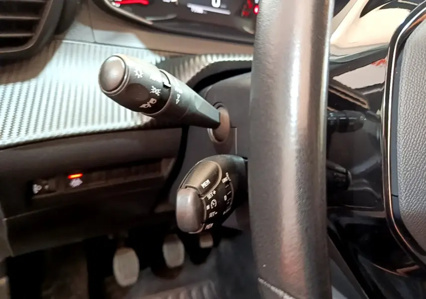 Gros plan sur les commandes derrière le volant cuir noir du Peugeot 2008 gris clair, tableau de bord texturé visible.