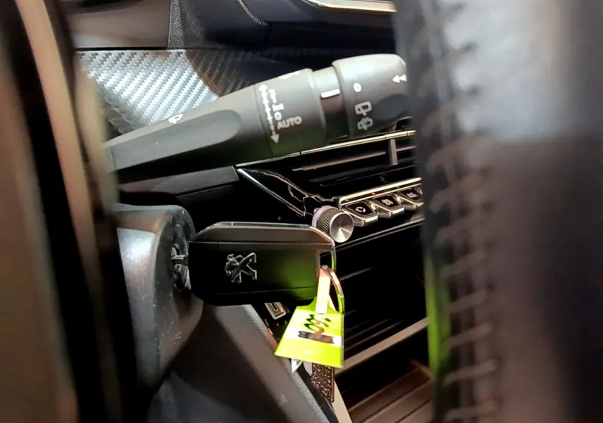 Gros plan sur la clé Peugeot insérée dans le contacteur, avec partie du tableau de bord et commandes visibles.