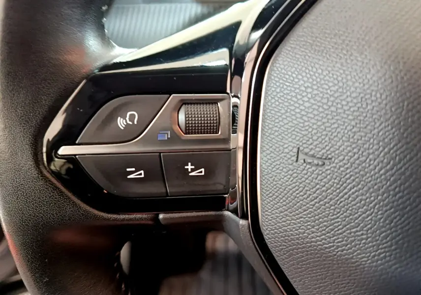 Gros plan sur les commandes vocales et volume du volant cuir noir du Peugeot 2008 gris clair 2020.
