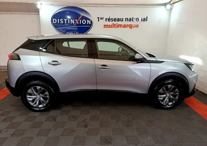 Profil côté droit d'un Peugeot 2008 gris clair 2020 dans un showroom avec logo Distinxion en arrière-plan.
