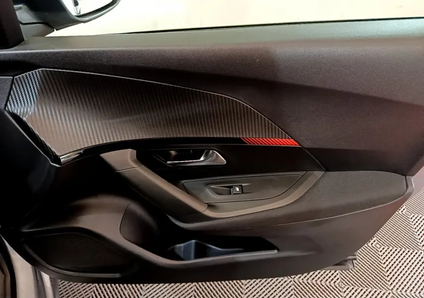 Gros plan sur la porte côté conducteur de la Peugeot 2008 gris clair, avec insert carbone et bande rouge décorative.