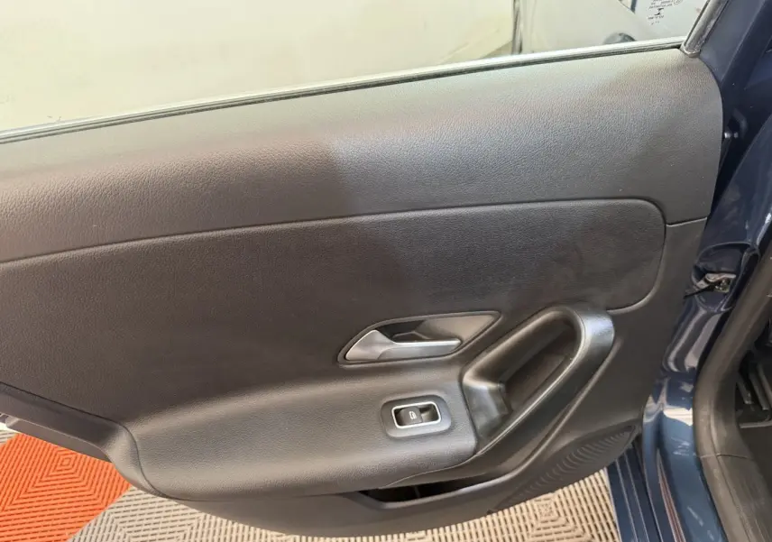 Vue rapprochée de la porte côté gauche d'une Mercedes Classe A 180 d Business Line bleu, avec poignée et bouton de vitre électrique.