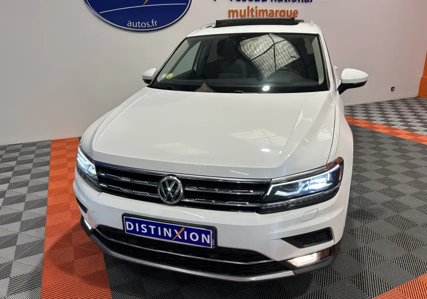 Vue 3/4 avant d'un Volkswagen Tiguan Allspace blanc avec phares LED allumés dans un showroom.