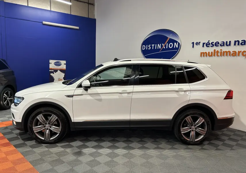 Profil latéral droit d'un Volkswagen Tiguan Allspace blanc 2018 avec jantes alliage et vitres teintées en showroom.