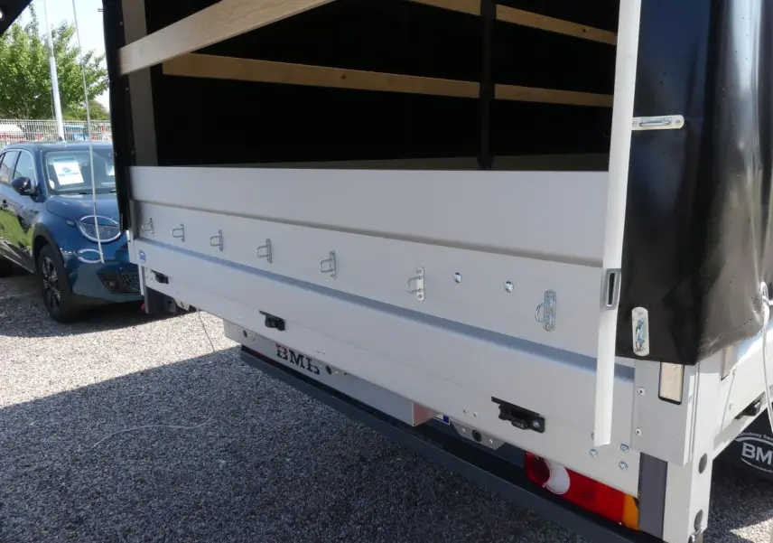 Vue arrière du Renault Master Extra gris avec bâche noire et ridelles métalliques blanches ouvertes sur un sol gravillonné.