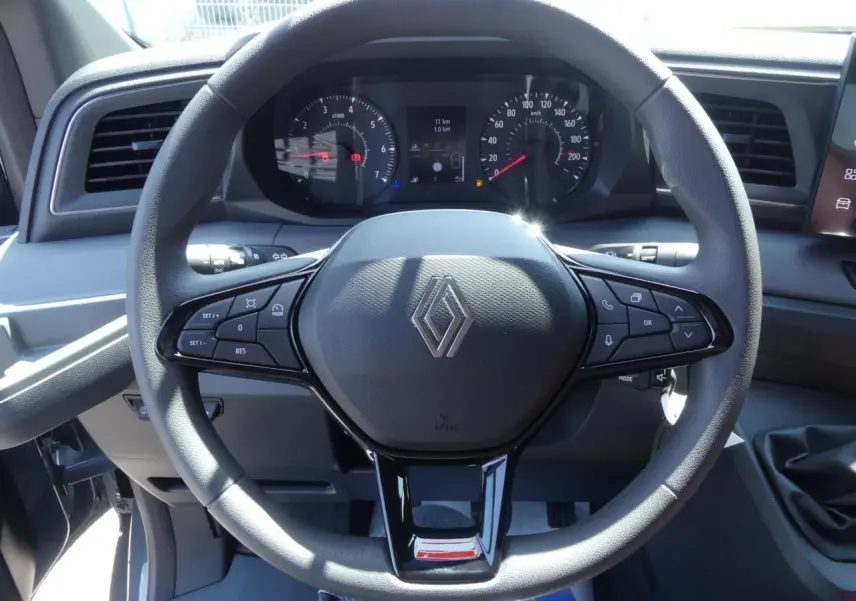 Vue rapprochée du volant noir du Renault Master 2025 avec commandes intégrées et tableau de bord digital en arrière-plan.