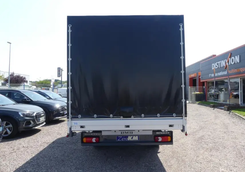 Vue arrière d'un Renault Master Extra gris avec bâche noire et feux arrière visibles sur un parking.