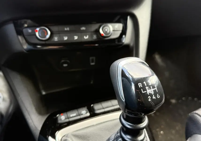 Le levier de vitesses manuel noir de l'Opel Corsa 1.2i Turbo 100 GS en gros plan avec console centrale en arrière-plan.