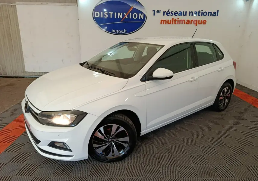Volkswagen Polo blanche vue en 3/4 avant droit, avec phares allumés et jantes alliage distinctives.