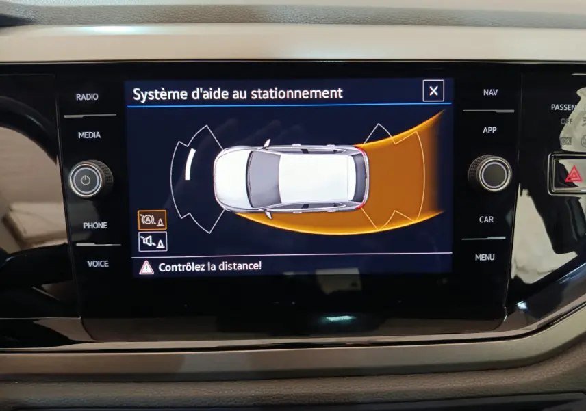 Écran tactile intérieur affichant l'aide au stationnement d'une Volkswagen Polo blanche vue de dessus.