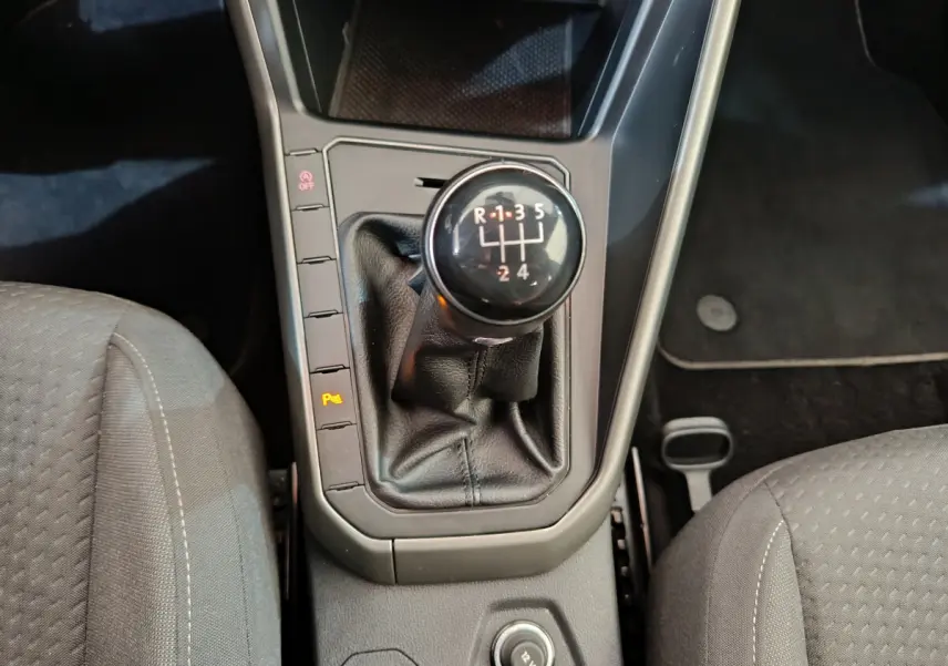 Gros plan sur le levier de vitesses manuel noir entouré des sièges avant gris du Volkswagen Polo 1.0 TSI 2020.