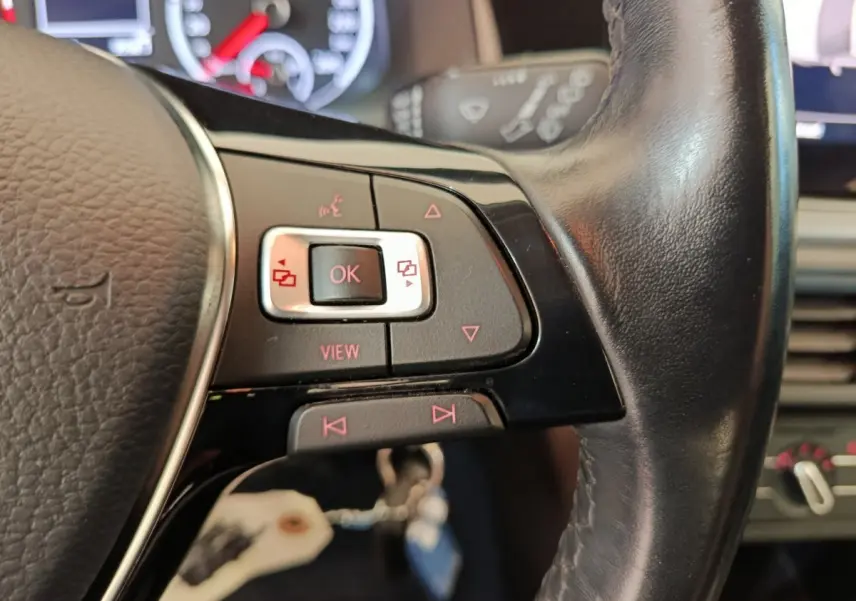 Gros plan sur les commandes gauche du volant cuir noir de la Volkswagen Polo blanche, tableau de bord en arrière-plan.