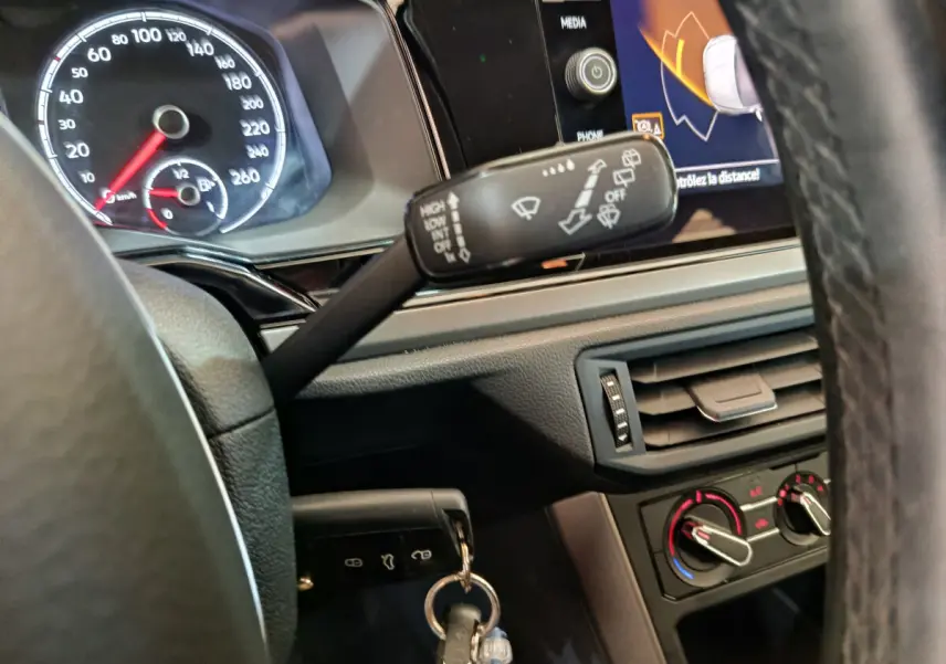 Vue rapprochée du tableau de bord et volant de la Volkswagen Polo blanche 2020, avec commandes d’essuie-glace et écran tactile visible.