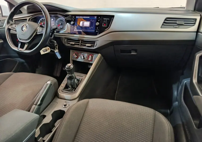 Intérieur avant de la Volkswagen Polo blanche 2020, tableau de bord avec écran tactile et boîte manuelle visible.