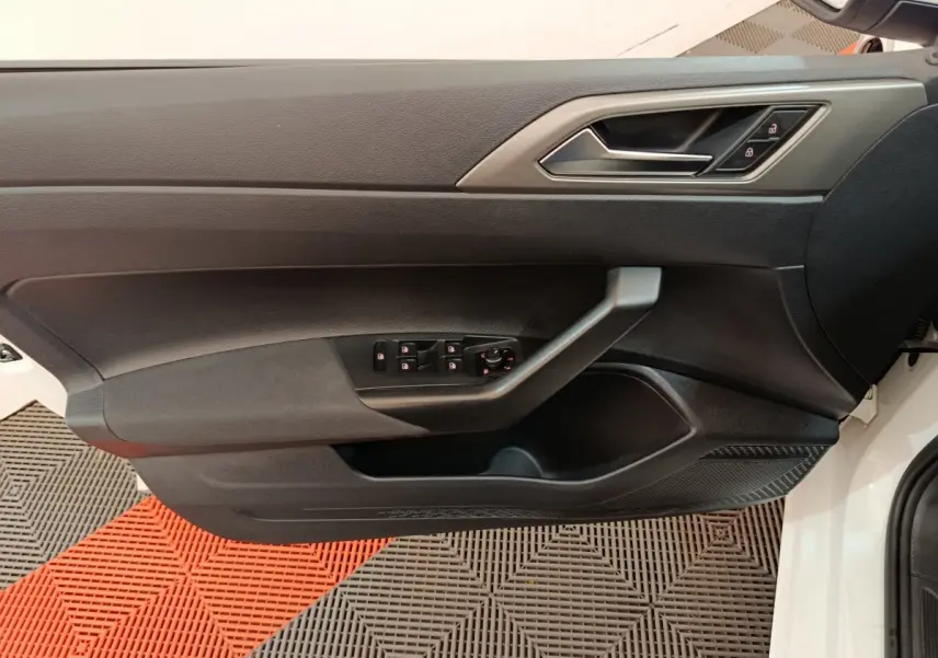 Vue rapprochée de la porte avant gauche noire d'une Volkswagen Polo blanche, avec commandes de vitres et serrure intégrées.