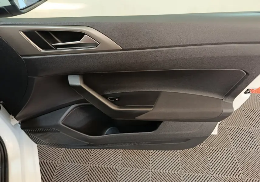 Vue rapprochée de la porte avant gauche noire d'une Volkswagen Polo blanche 2020, avec poignée intégrée et rangements.