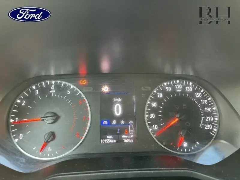 Tableau de bord Ford avec compte-tours et compteur de vitesse analogiques, affichage digital au centre, éclairage rouge et blanc.