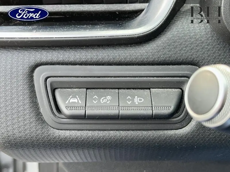 Gros plan sur les commandes d'assistance au conducteur dans une Renault Clio gris platine, avec boutons de réglage et molette.