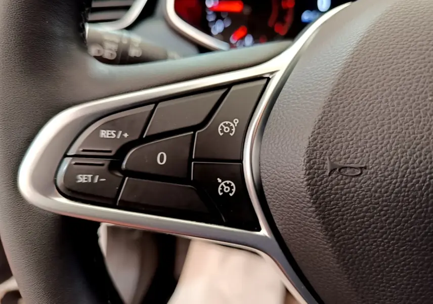 Gros plan sur les commandes de régulateur de vitesse au volant cuir noir d'une Renault Clio Business Blue dCi blanche.